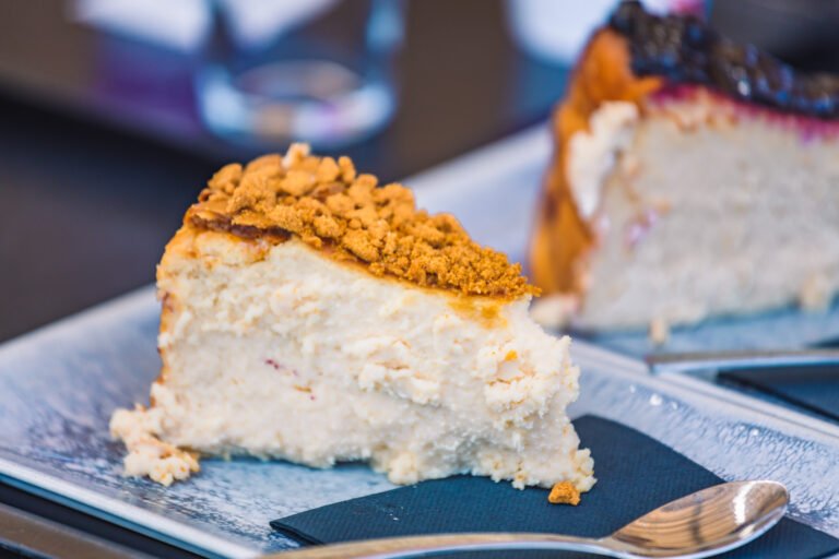 Tarta de queso con cobertura crujiente servida en un plato azul, acompaÃ±ada de una cuchara sobre una servilleta negra.