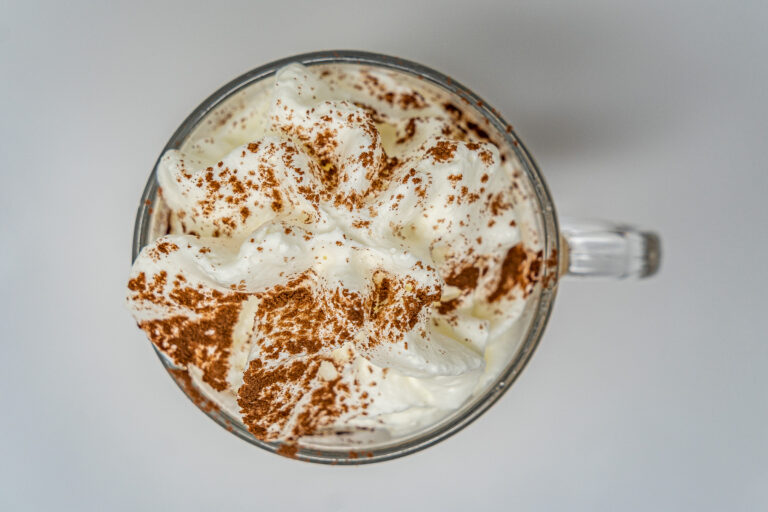 Taza de chocolate caliente con crema batida y espolvoreado de cacao visto desde arriba
