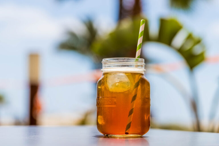 TÃ© helado en tarro de cristal con pajita verde y blanca, fondo de palmeras y cielo azul en My Sweet, Costa Azahar
