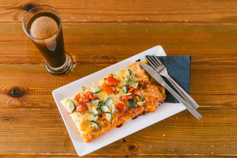 Tarta salada con verduras y tenedor sobre servilleta negra, junto a vaso de bebida espumosa en mesa de madera