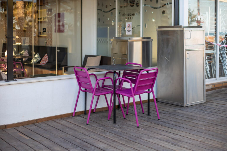 Terraza con sillas moradas y mesa negra en My Sweet, junto a fachada de cristal y suelo de madera.