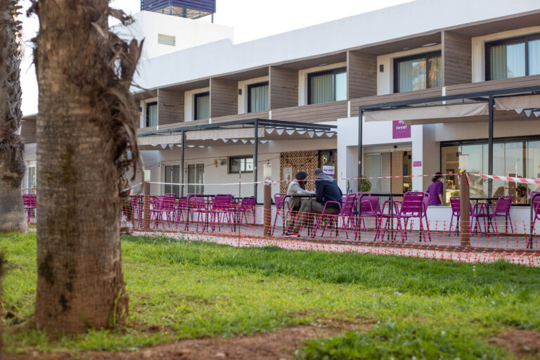 Terraza de cafeterÃ­a My Sweet con mesas y sillas moradas, vista lateral del edificio del hotel Costa Azahar.