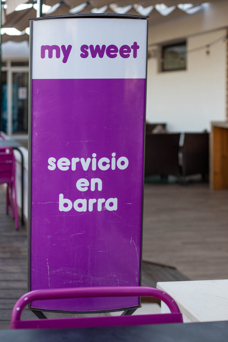 Cartel morado de My Sweet con texto "servicio en barra" en terraza al aire libre.