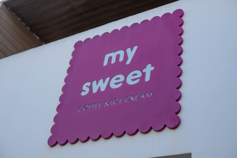 Letrero rosa de "My Sweet" con borde ondulado, letras blancas, sobre pared blanca.