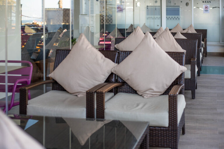 SofÃ¡s de mimbre con cojines beige en terraza de cafeterÃ­a junto a mesas de cristal