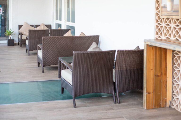 Terraza de cafeterÃ­a con sillones de mimbre marrÃ³n y cojines beige, mesa de cristal y decoraciÃ³n moderna.