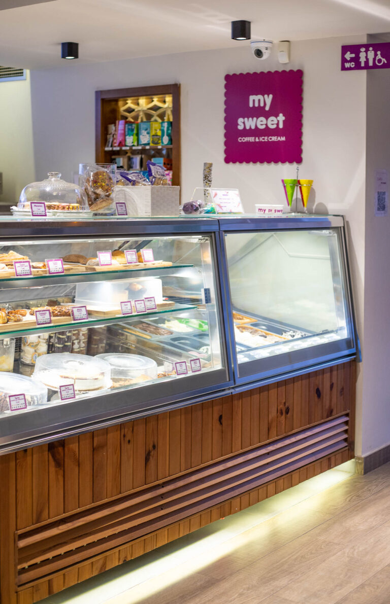 Mostrador de pastelerÃ­a y helados en My Sweet, con dulces exhibidos y letrero rosa en la pared.
